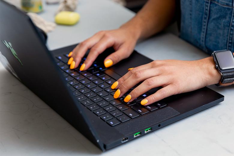 A woman's hands with yellow nail polish typing on a laptop. 