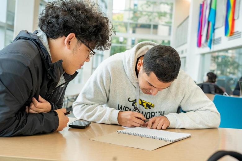 Two students write in a notebook in the Beatty Campus Center