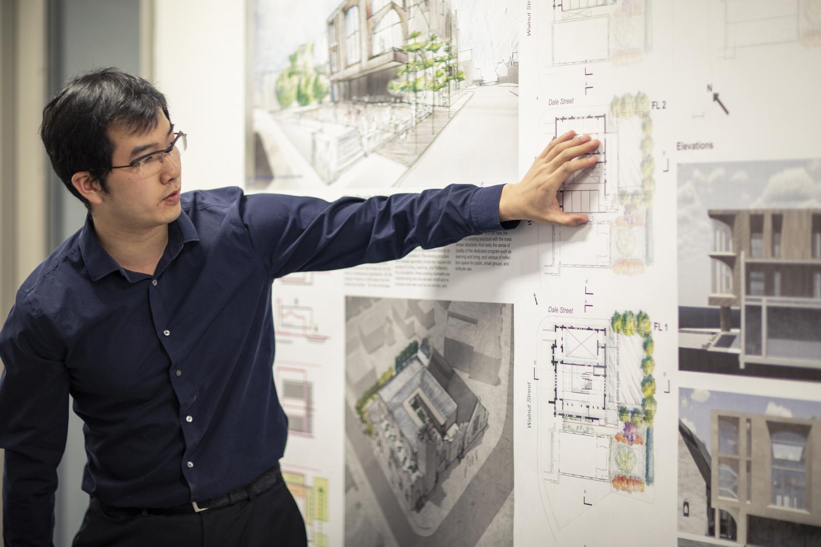 Masters student pointing to poster presentation on architecture designs