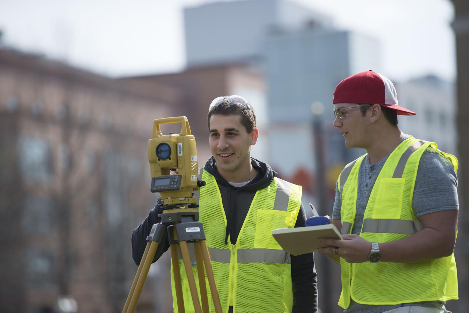 Two students wearing bright vests practice surveying in Boston