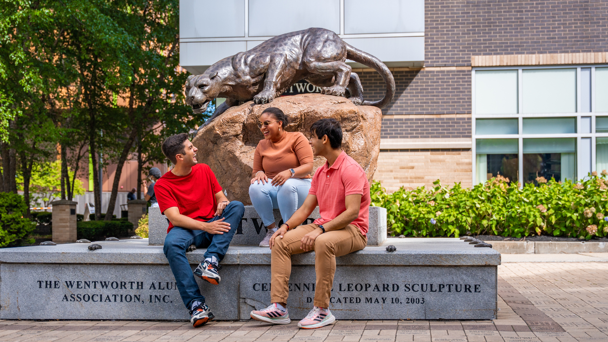 Three students laugh while sitting on the base of the Wentworth Leopard Statue