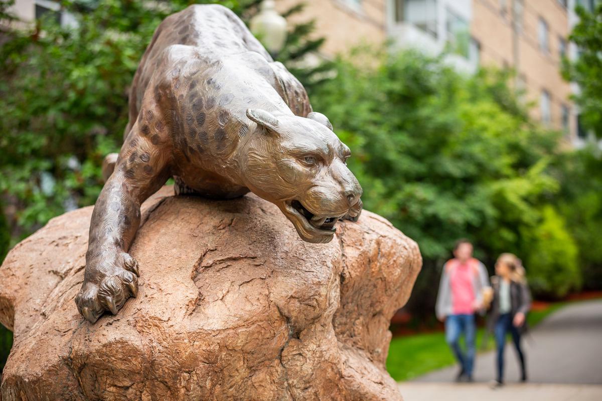 The Wentworth leopard statue with two students walking by in the background on an autumn day