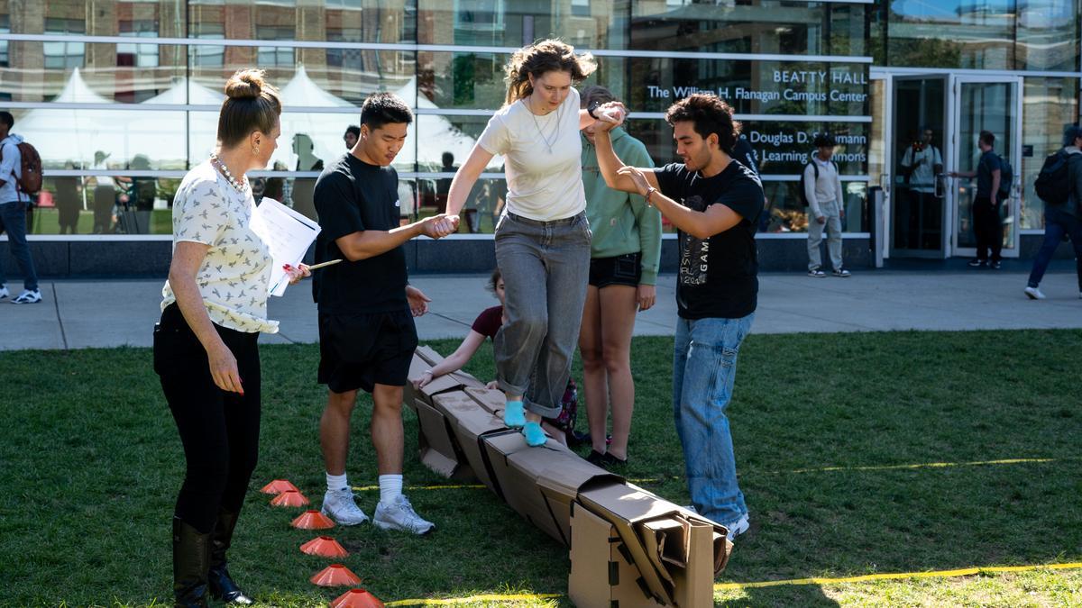 Industrial Design students build a bridge out of cardboard and help a woman walk across it on the quad.