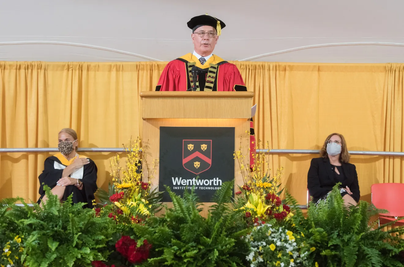 man speaking at a podium in graduation robe