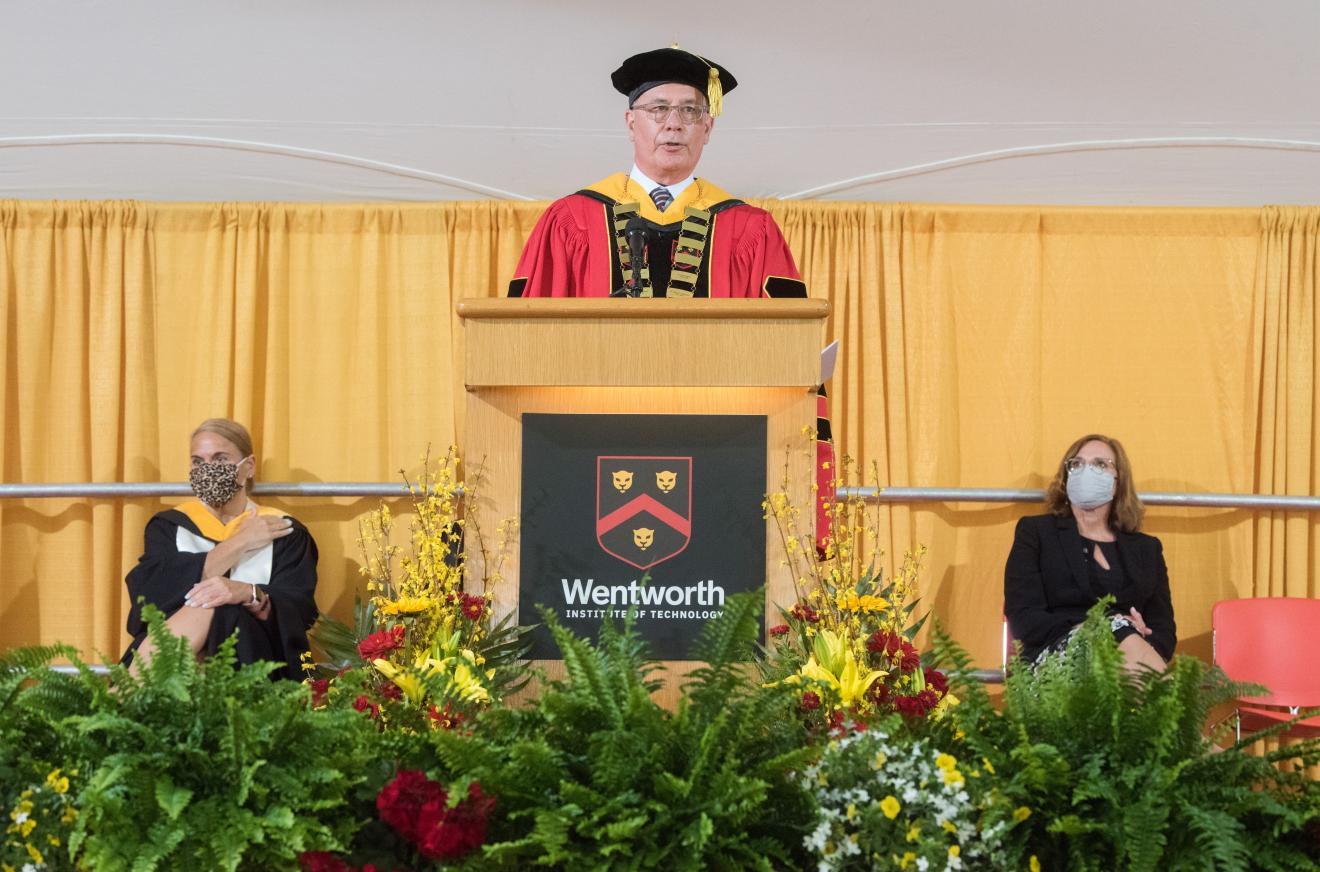 man speaking at a podium in graduation robe