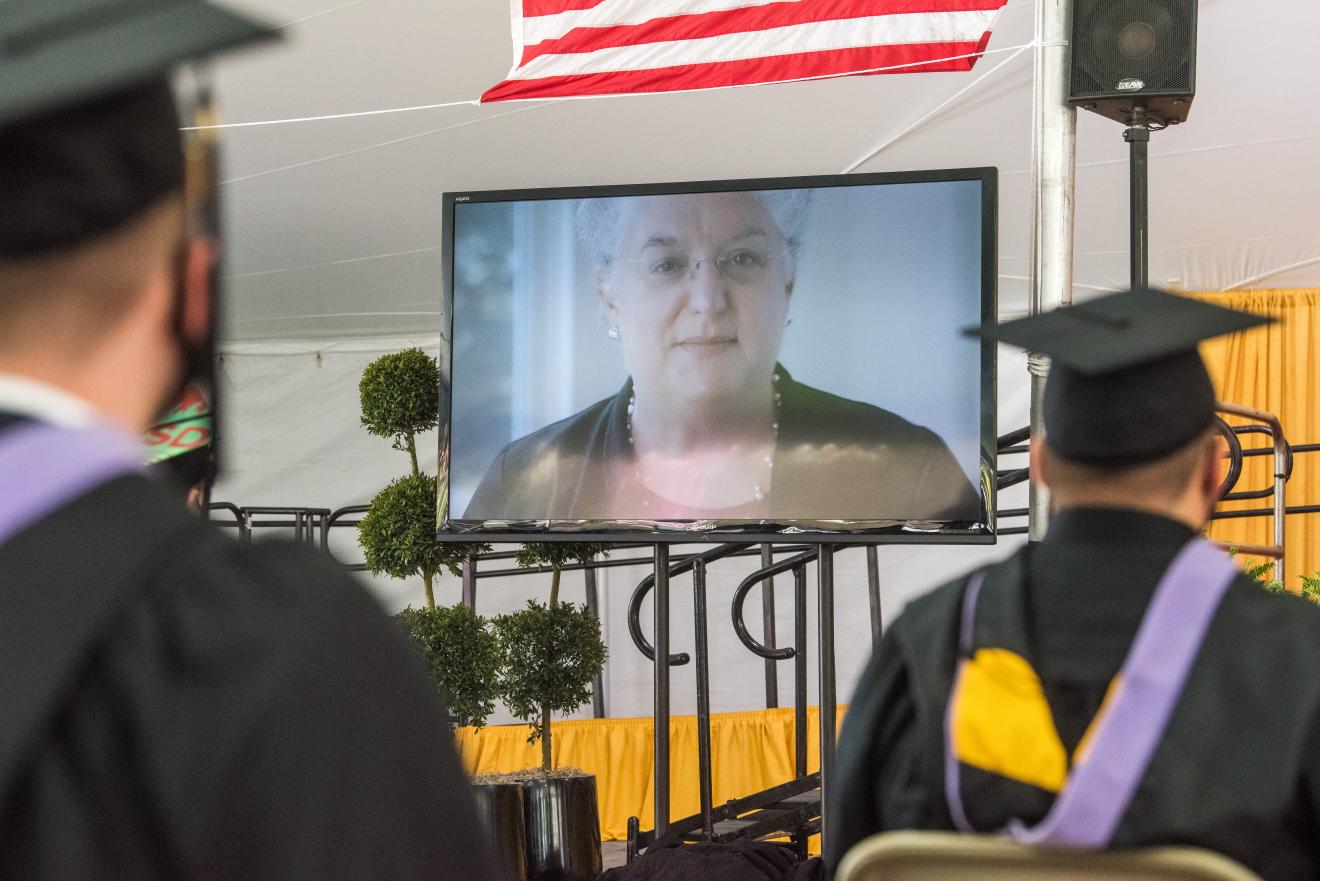 woman shown on big screen as graduates look on
