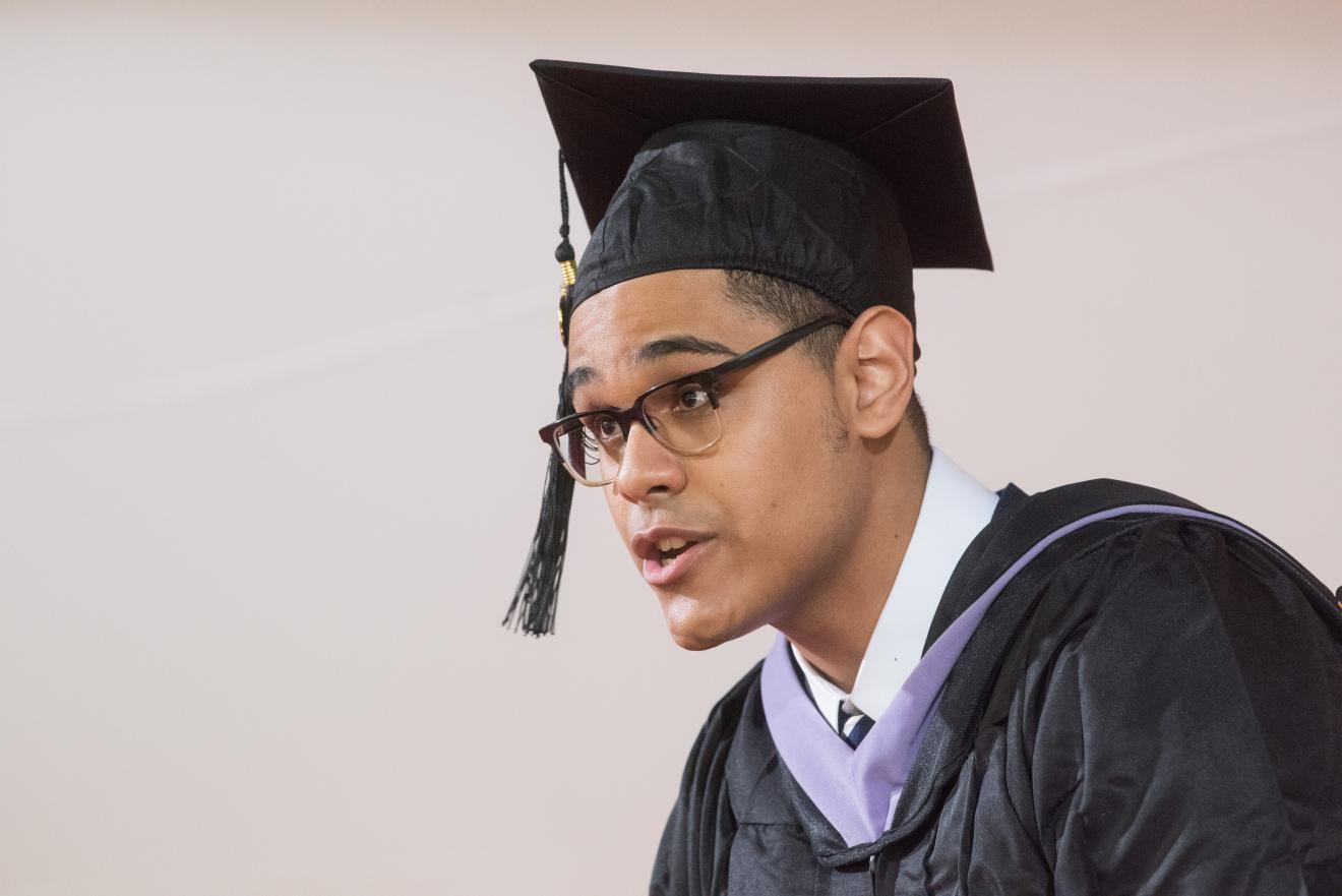 man speaks while wearing graduation cap