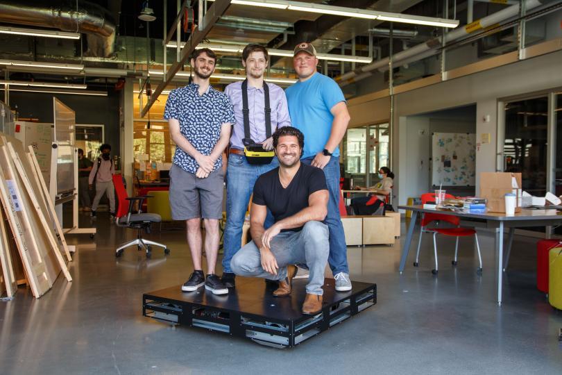 four men pose next to a robot pallet