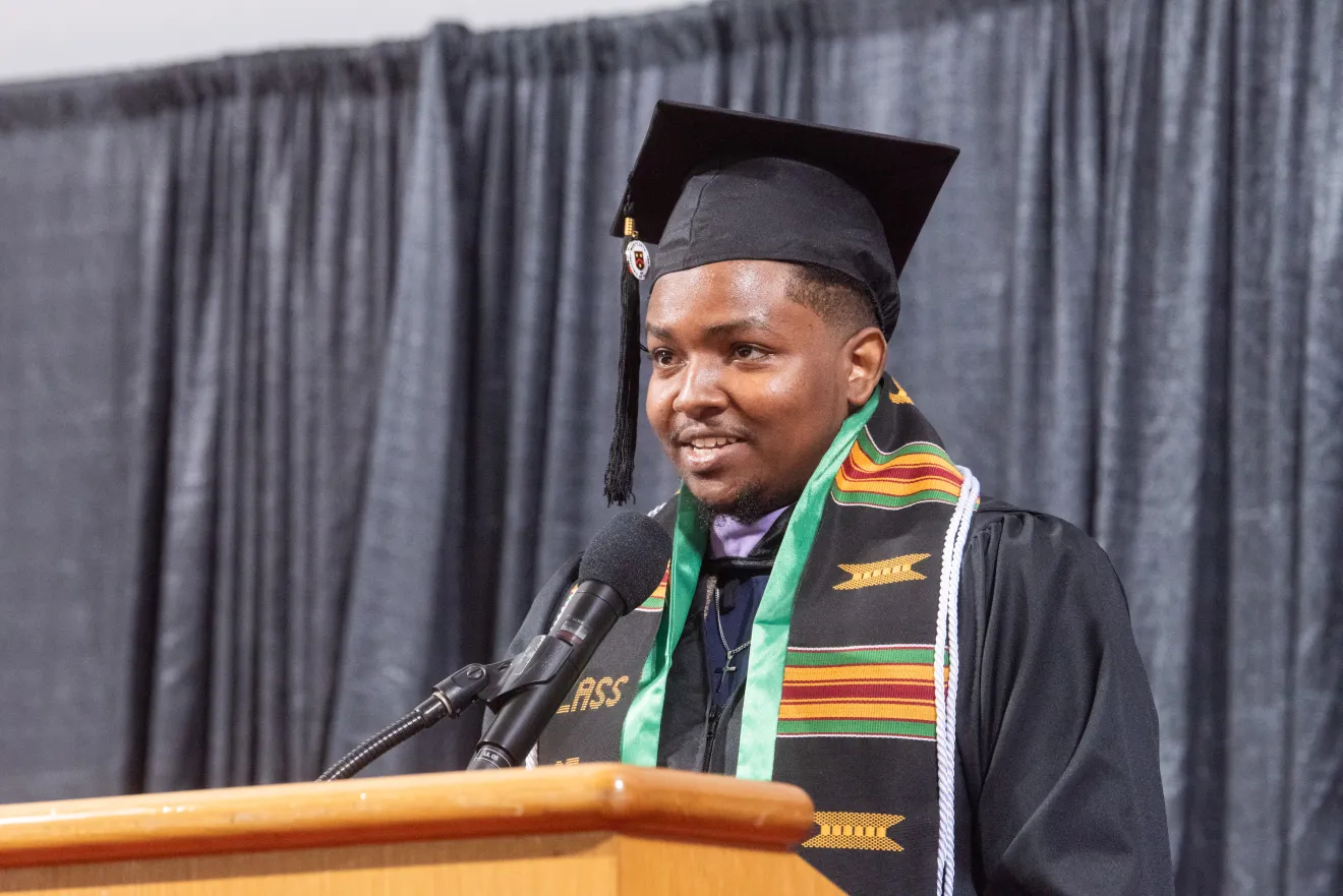 a man speaking at a podium and wearing a graduation robe