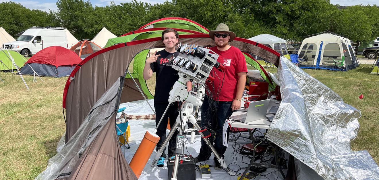 Two people outdoors in a tent with a telescope