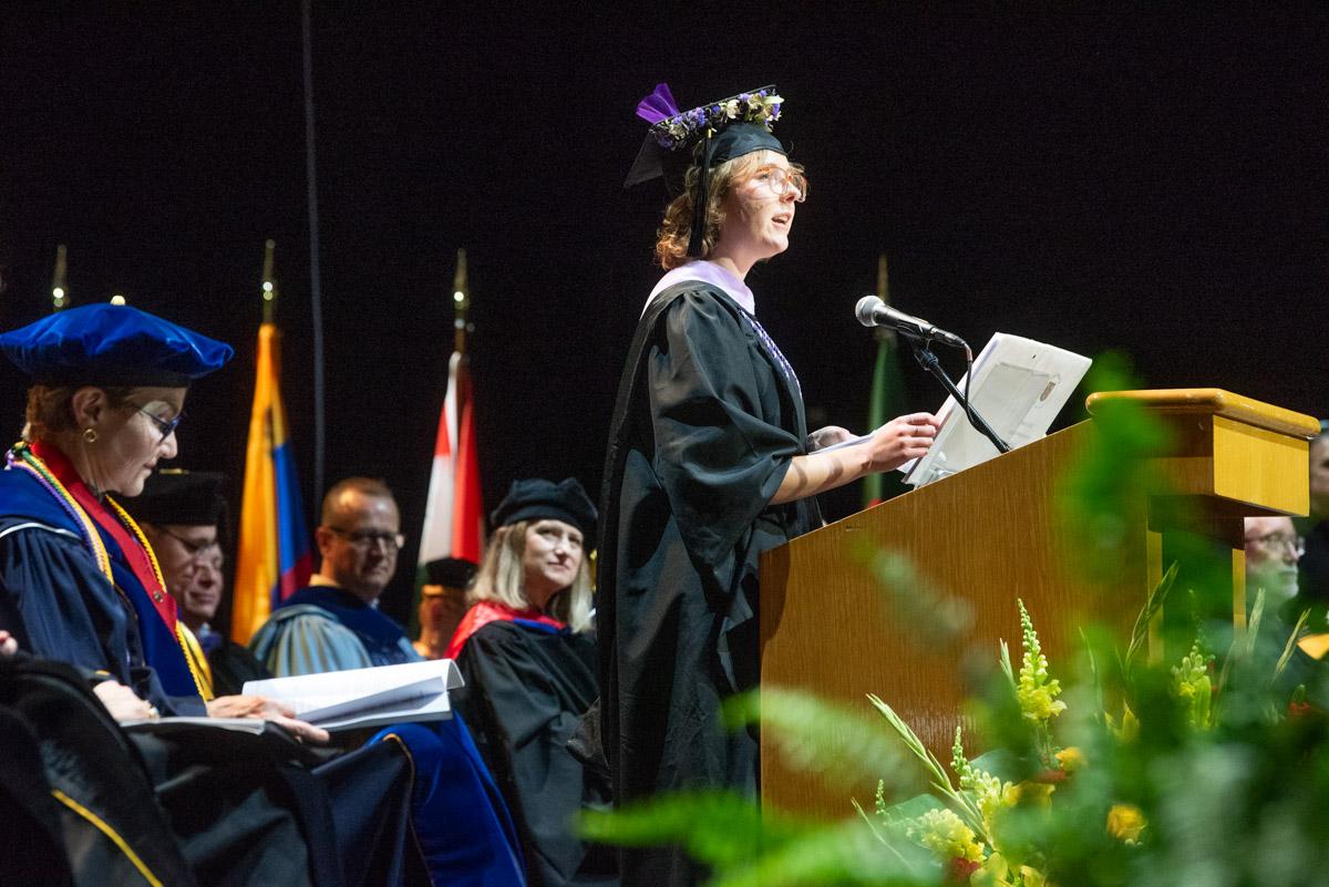 a woman in a graduation cap and gown speaks at a podium