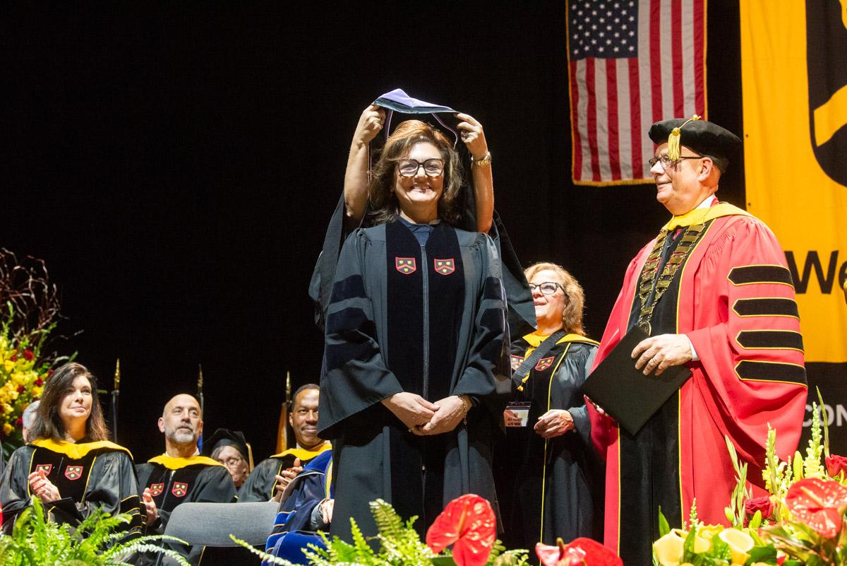 a woman stands on stage in a graduation robe