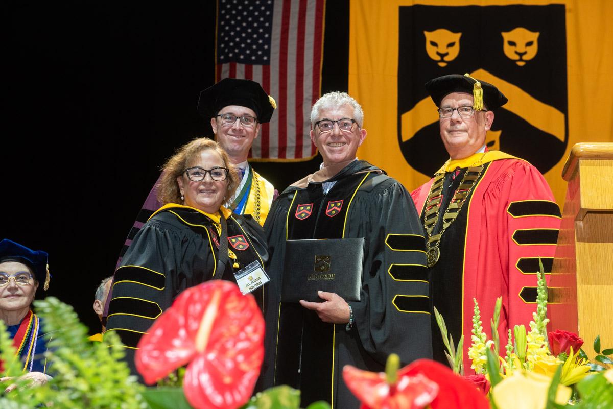 several people stand on a stage in graduation robes