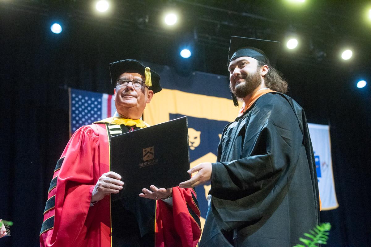 two men stand in graduation robes