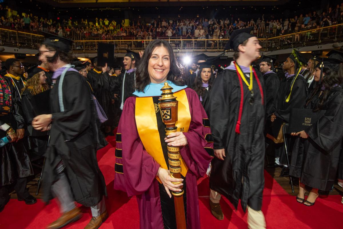 a woman in a red robe leads a graduation procession