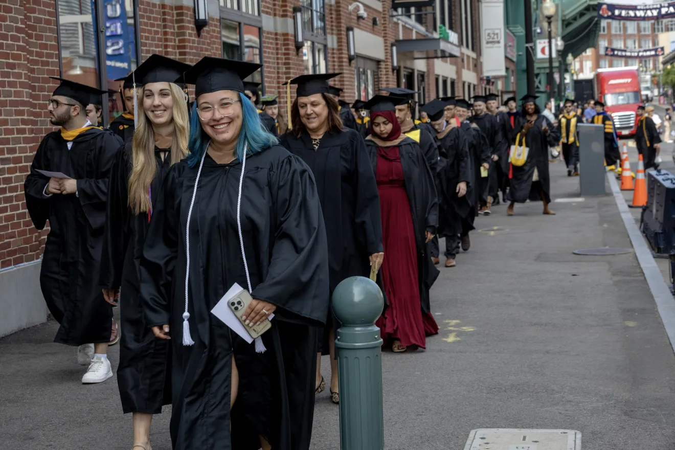 people in graduation gowns lining up on a sidewalk in boston