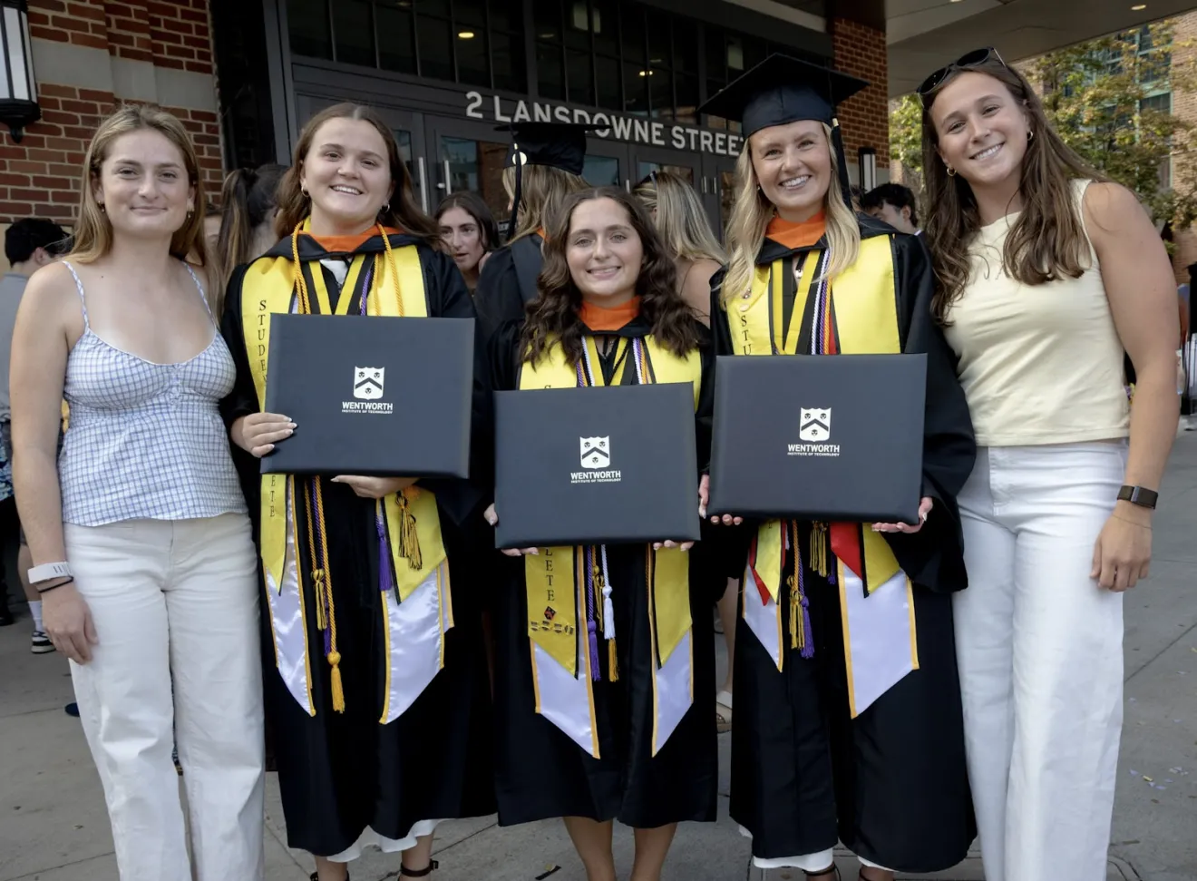 women in graduates caps and gowns pose with friends