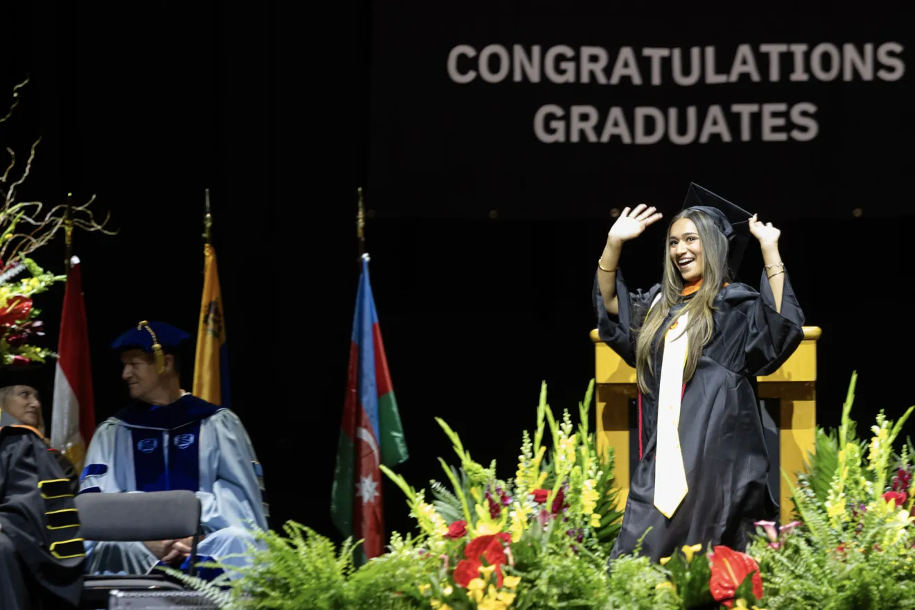 a woman in a graduation robe crosses a stage