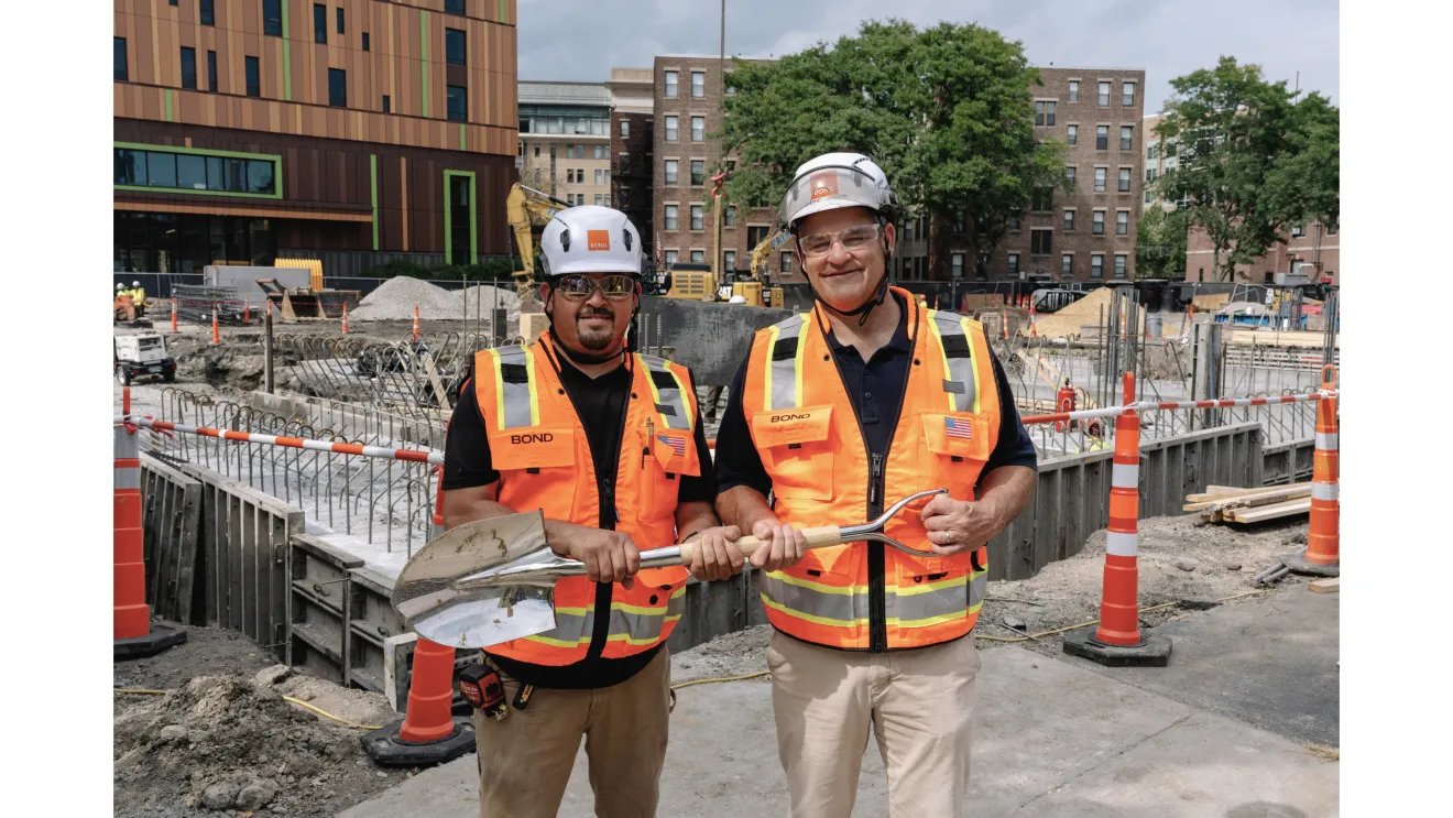 Two people wearing orange construction vests and hard hats