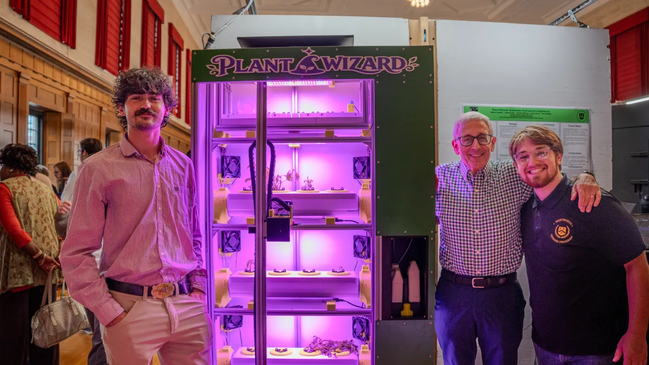 three people stand beside a purple device used for growing plants