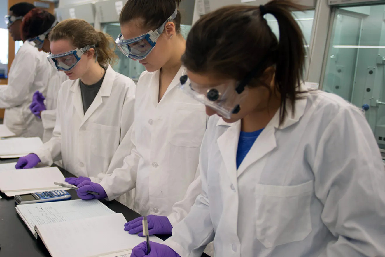 Women in lab gear working on class notes.