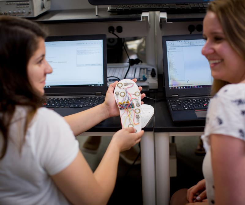 Two students work on programming a medical device in the lab