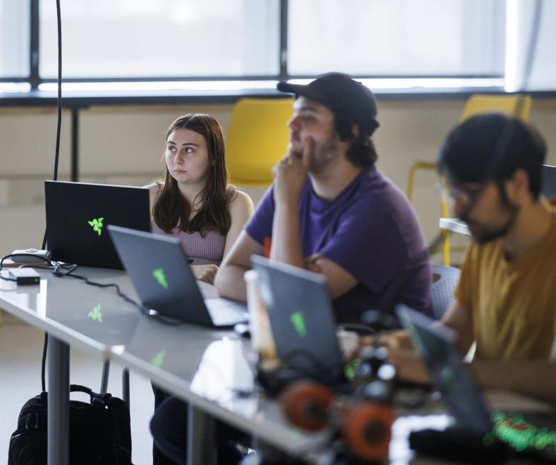 Three students sit at tables in the Computing & Data Science classroom during a lecture