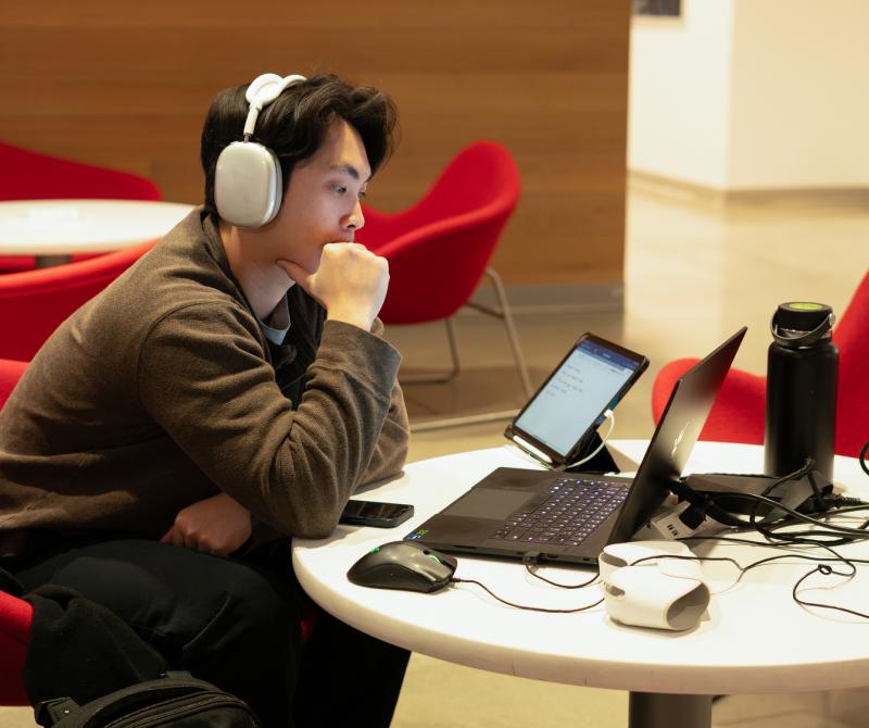 A student sits in the CEIS lobby with his headphones on while studying on his laptop