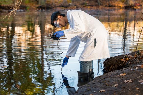 A male student uses a handheld instrument to test a body of water in Boston.