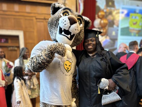 a woman in a graduation robe poses with a leopard mascot