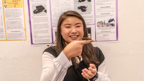 a woman holds up a cockroach fitted with a sensor