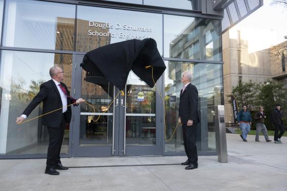 two men remove a covering on a building to reveal a new sign