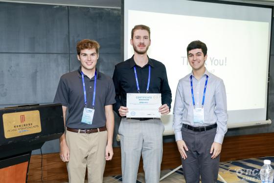 three students stand while one holds a certificate