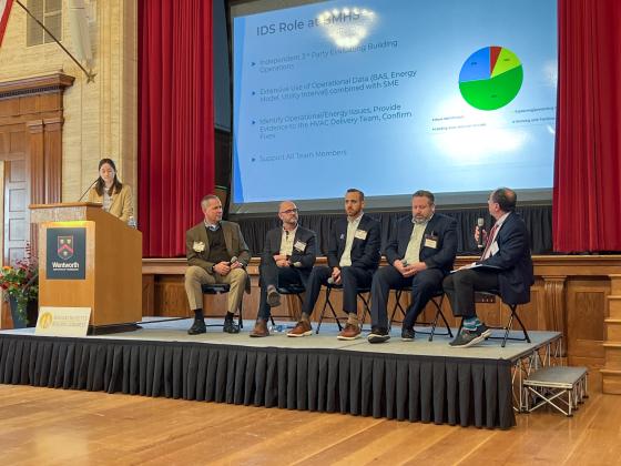 four people sit on a stage as part of a panel while a moderator stands at a podium