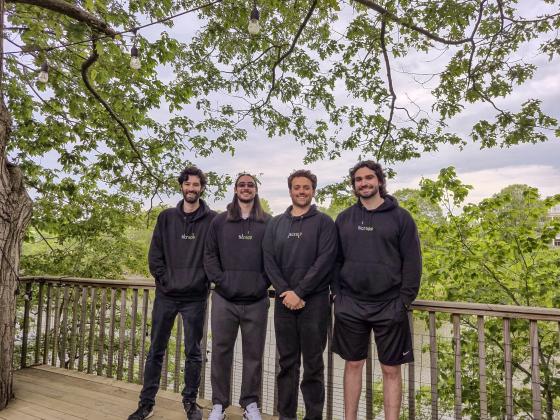 a group of four people pose in black sweatshirts in front of trees