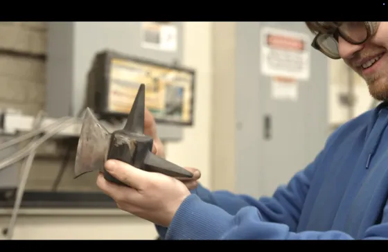 a student holds up a steel axe part