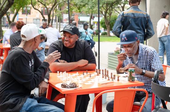 three men having a chat over a chess board outdoors