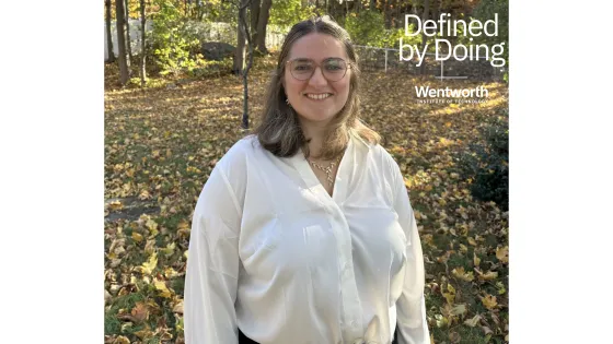 a woman wearing glasses stands in a wooded area