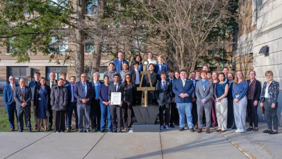 a large group of people pose in front of a statue on a college campus