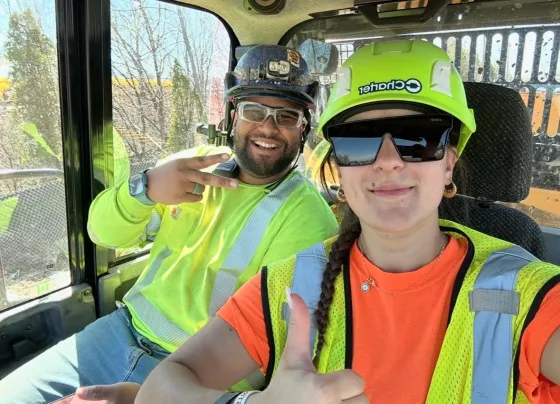 two people in hard hats and vests witting in an excavator