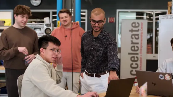 students and a professor look at a computer screen together