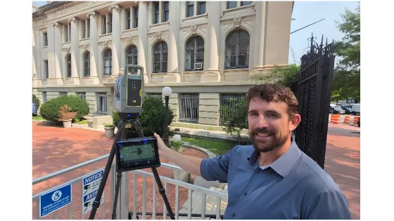 a man stands with a 3d scanner in front of a beaux-arts style building