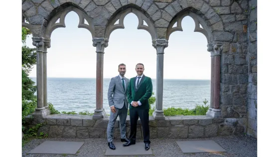 two men standing in front of large windows overlooking the water