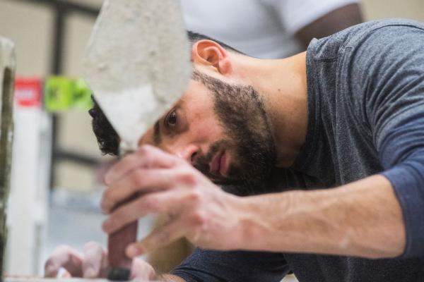 A bearded man uses a trowel to complete a construction project.
