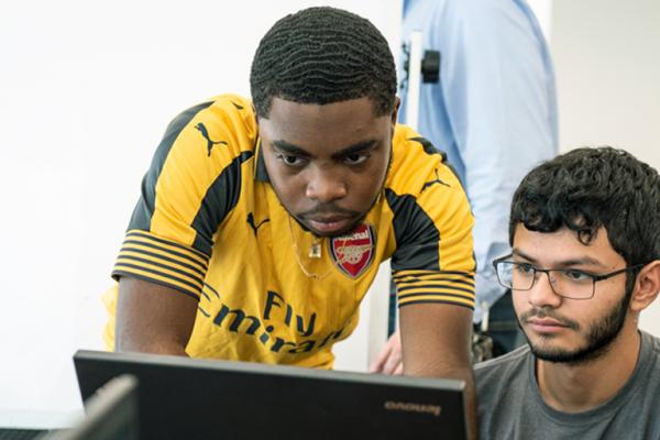 Two male students look at a laptop. 