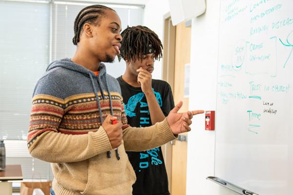 Two male, black students working at a whiteboard.
