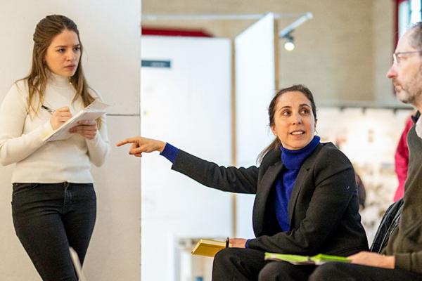 A professor gestures while looking a man as a student stand nears by and takes notes.