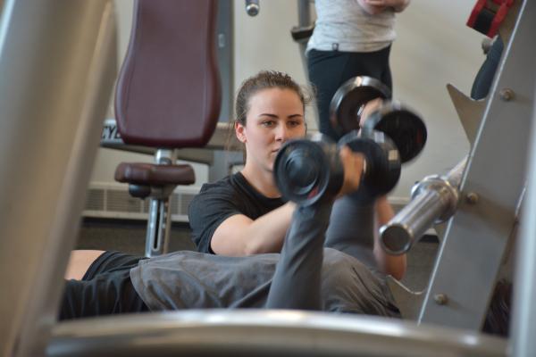 A female trainer is assisting a student lifting weights in the gym.