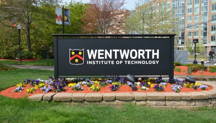 The main Wentworth sign surrounded by flowers at the corner of Ruggles and Huntington Aves