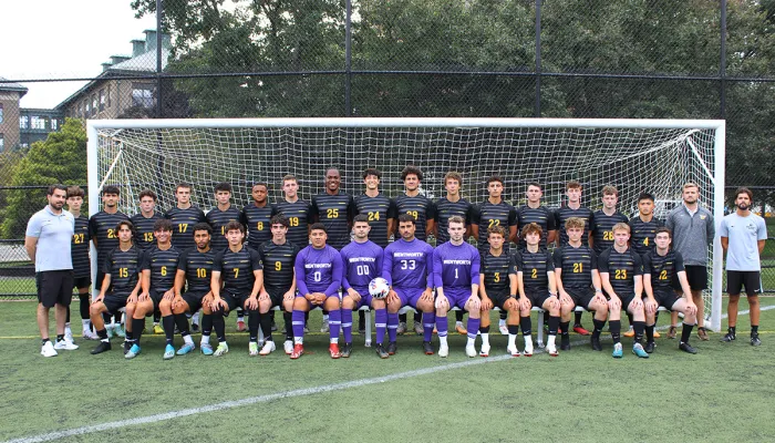 The men's soccer team poses in front of a goal on the soccer field